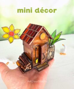 Handcrafted stained glass house featuring a small garden bed for flowers, with a vibrant yellow bloom in the background — perfect stained glass garden art accent.