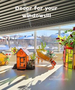 A collection of 3d stained glass pieces on a windowsill: a garden wheelbarrow with succulents, a mini birdhouse, a garden cottage, and a house-shaped flower pot holder, all glowing in natural light.