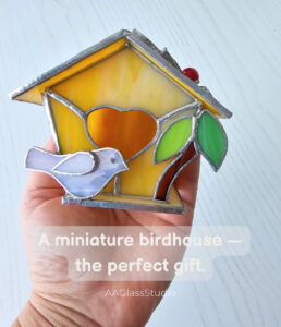 Miniature stained glass birdhouse wedding gift held in hand with purple bird, yellow walls and heart design by AAGlassStudio