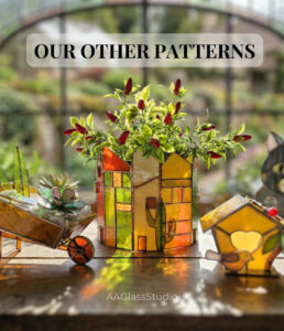 Handcrafted 3d stained glass pieces arranged on a windowsill: a garden wheelbarrow with succulents, a tiny birdhouse, and a house planter, showcasing vibrant glass art.