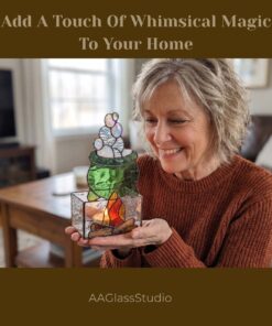 A smiling mature woman holds a handcrafted stained glass candle holder in the shape of a green cauldron with iridescent bubbles and a glass fire base which has a lit candle inside.