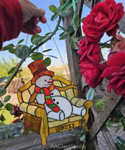 Boss Snowman stained glass suncatcher - hanging on a wooden trellis next to red roses, backlit by the sun