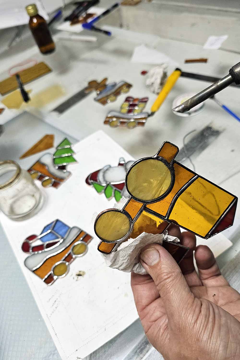 Artisan soldering the copper foil edges of a stained glass Christmas train piece in the AAGlassStudio workshop