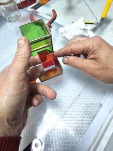 Assembling the red stained glass boiler section onto the green locomotive body with pliers, before the seams are soldered