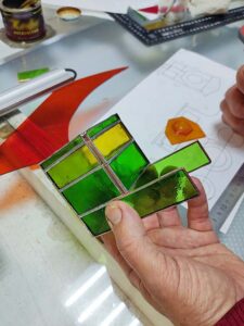 Soldered stained glass locomotive side panel with a green cab, yellow windows and the red boiler piece attached