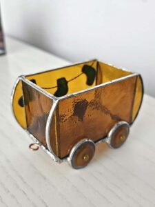 Amber and brown textured stained glass train wagon with round wheels standing on a white wooden table