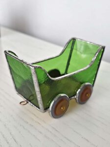 Finished green stained glass train wagon with round amber wheels and a copper coupling ring at the end